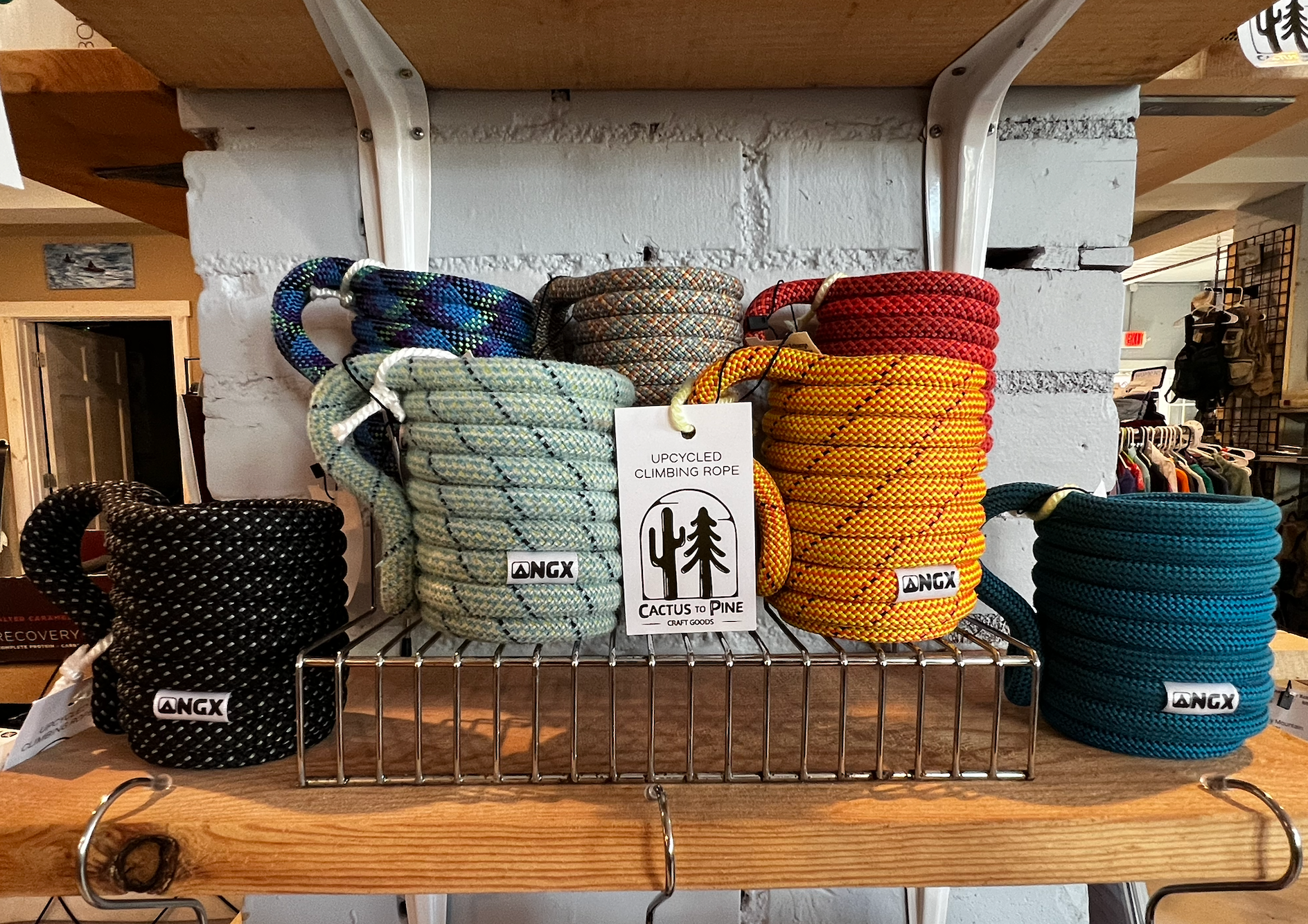 Upcycled climbing rope mugs by Cactus to Pine displayed on a wire rack in assorted colors including black, mint, blue, orange, red, and teal.